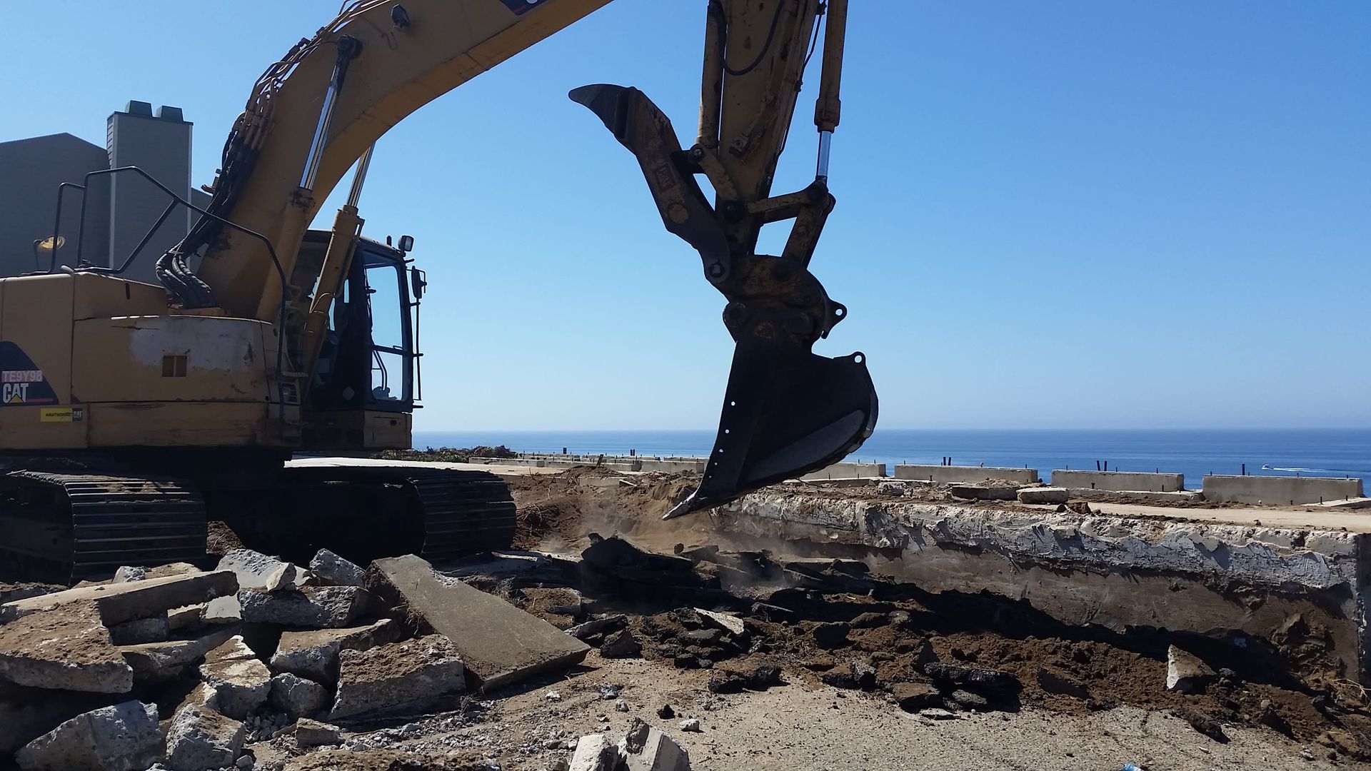 A cat excavator is digging in the dirt near the ocean.