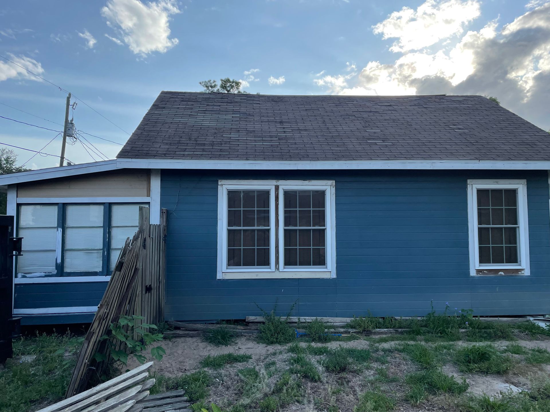A blue house with a roof and windows is sitting in the middle of a field.