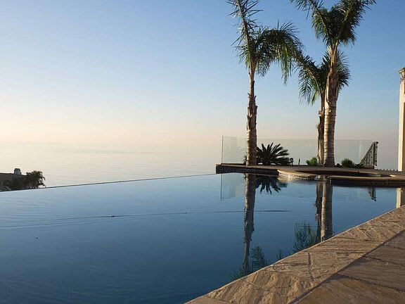 A swimming pool with a view of the ocean and palm trees.