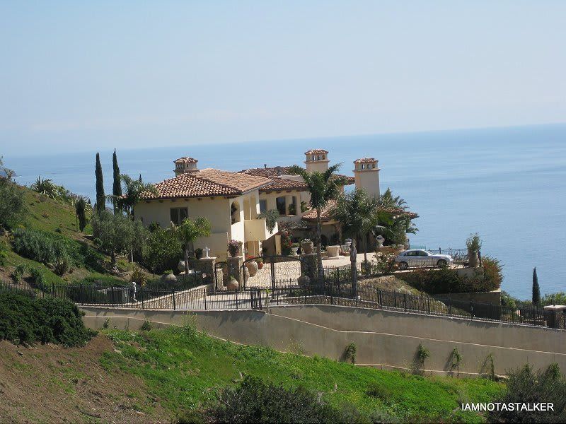 A large house sits on top of a hill overlooking the ocean.
