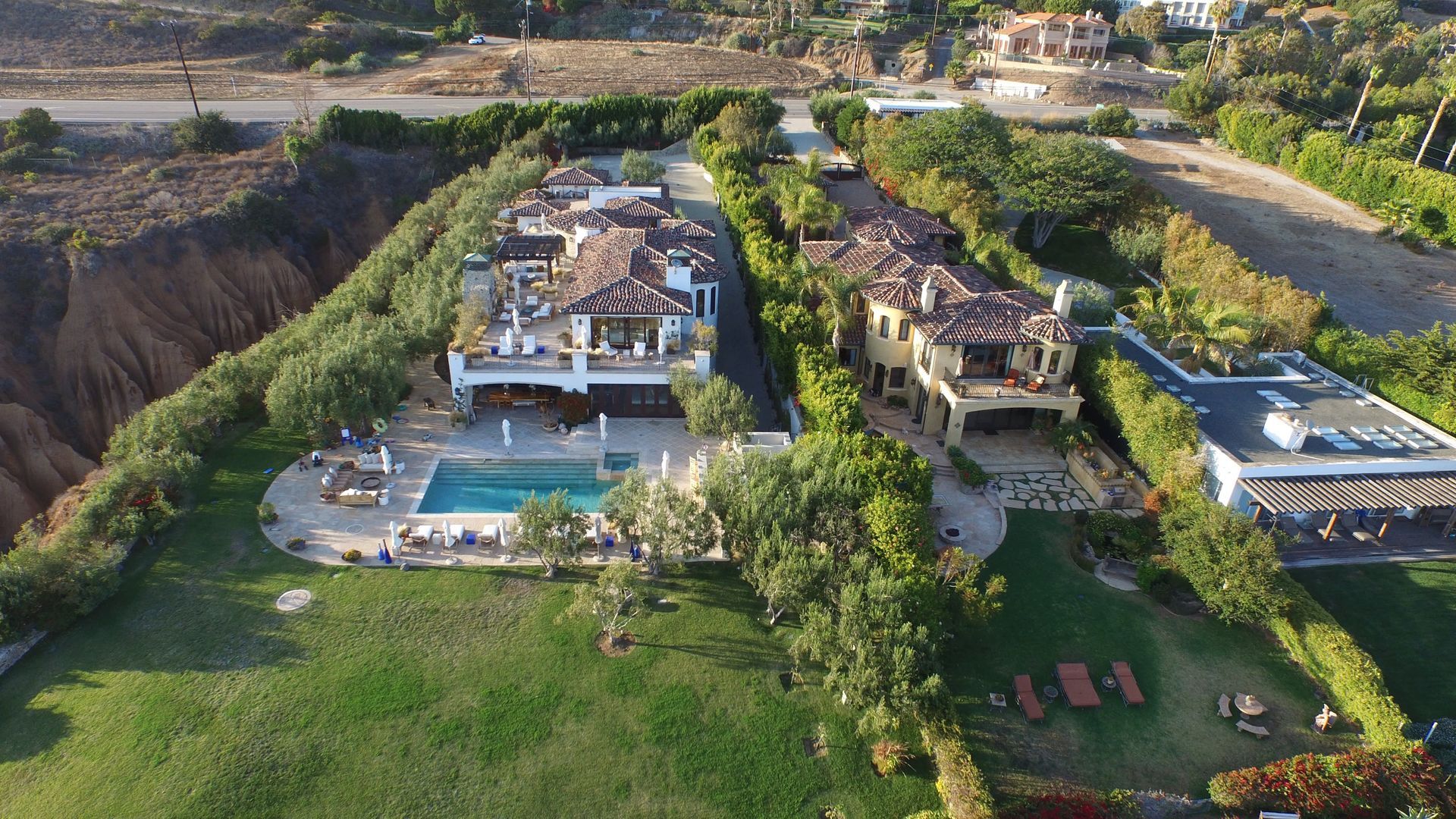 An aerial view of a large house with a pool in the middle of a lush green field.