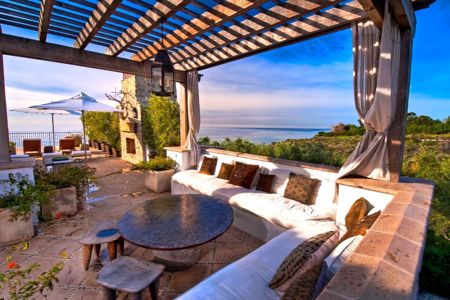 A patio with a couch and a table under a pergola overlooking the ocean.