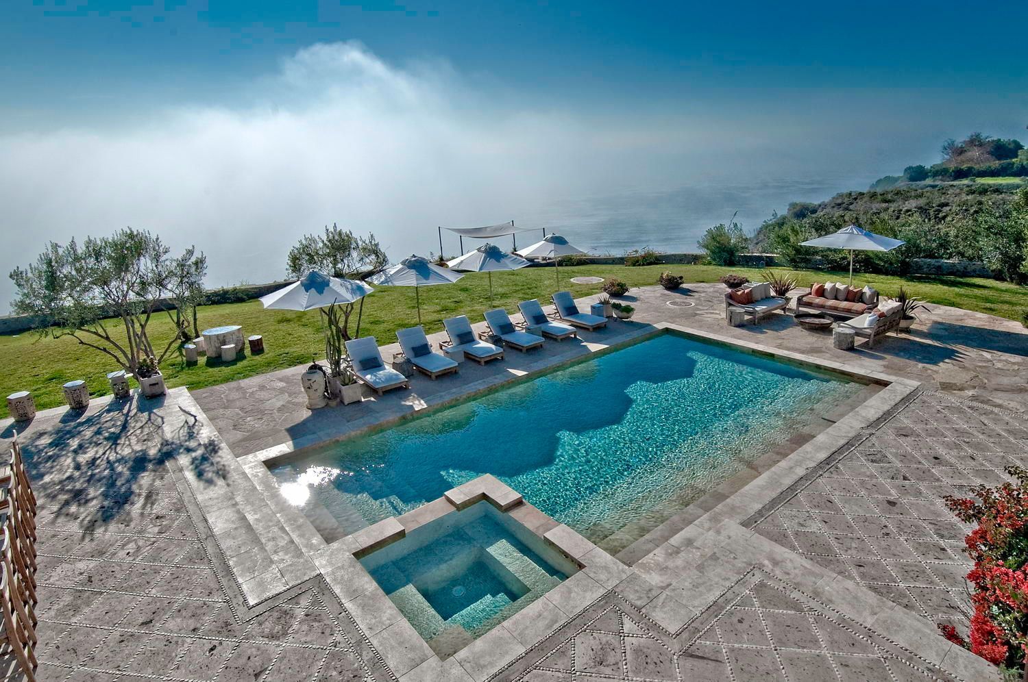 A large swimming pool surrounded by chairs and umbrellas with a view of the ocean.