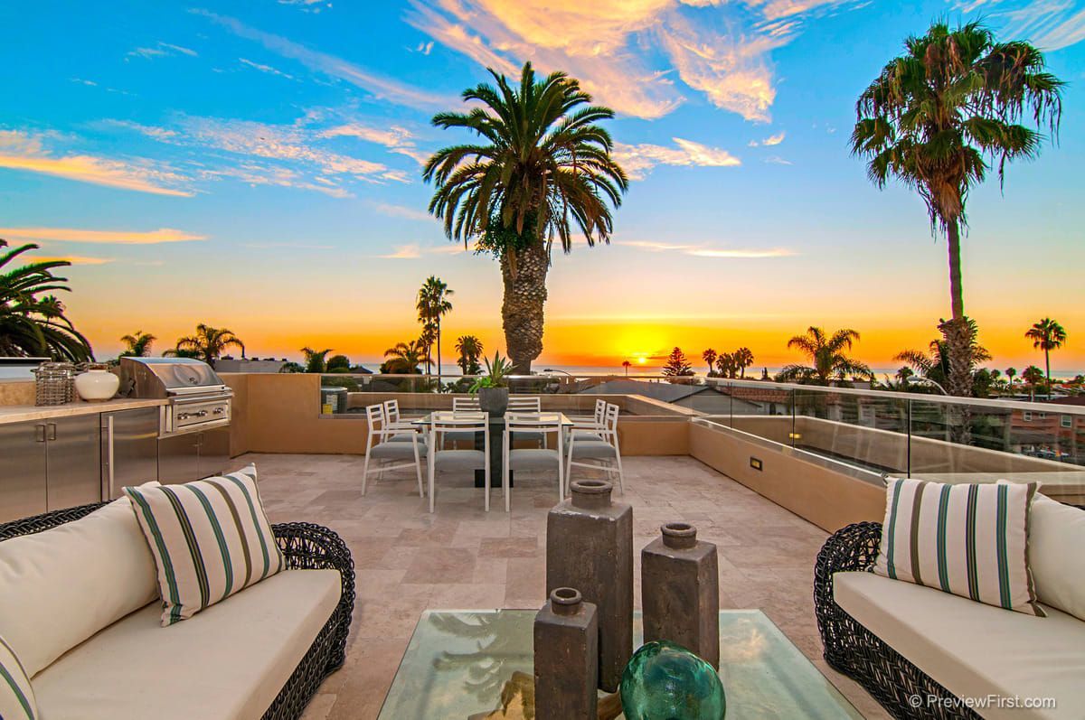 A patio with a table and chairs and a view of the ocean at sunset.
