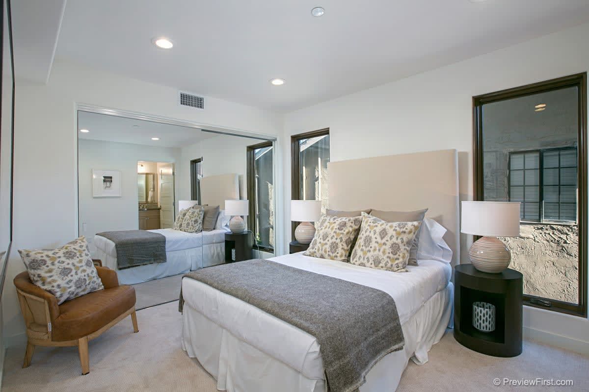 A bedroom with a large bed , chair , lamps and mirrors.