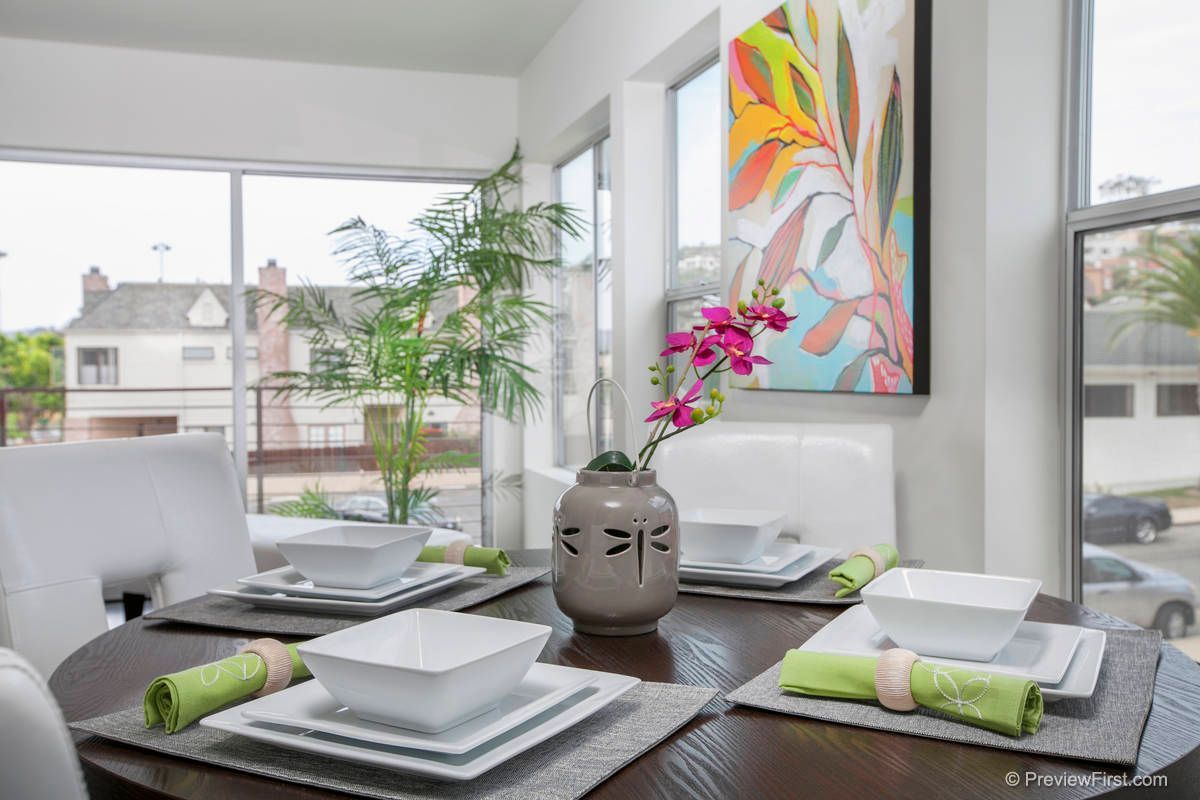 A dining room table with plates , bowls , and a vase of flowers.