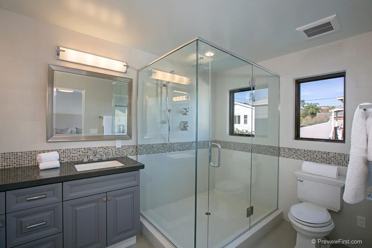 A bathroom with a walk in shower , sink , toilet and mirror.