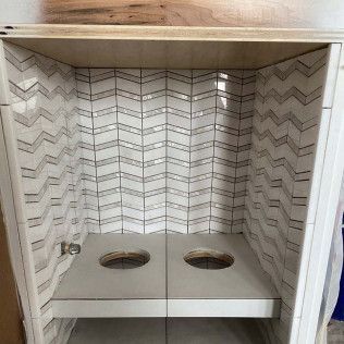 Bathroom vanity with herringbone tile backsplash and two sink holes.