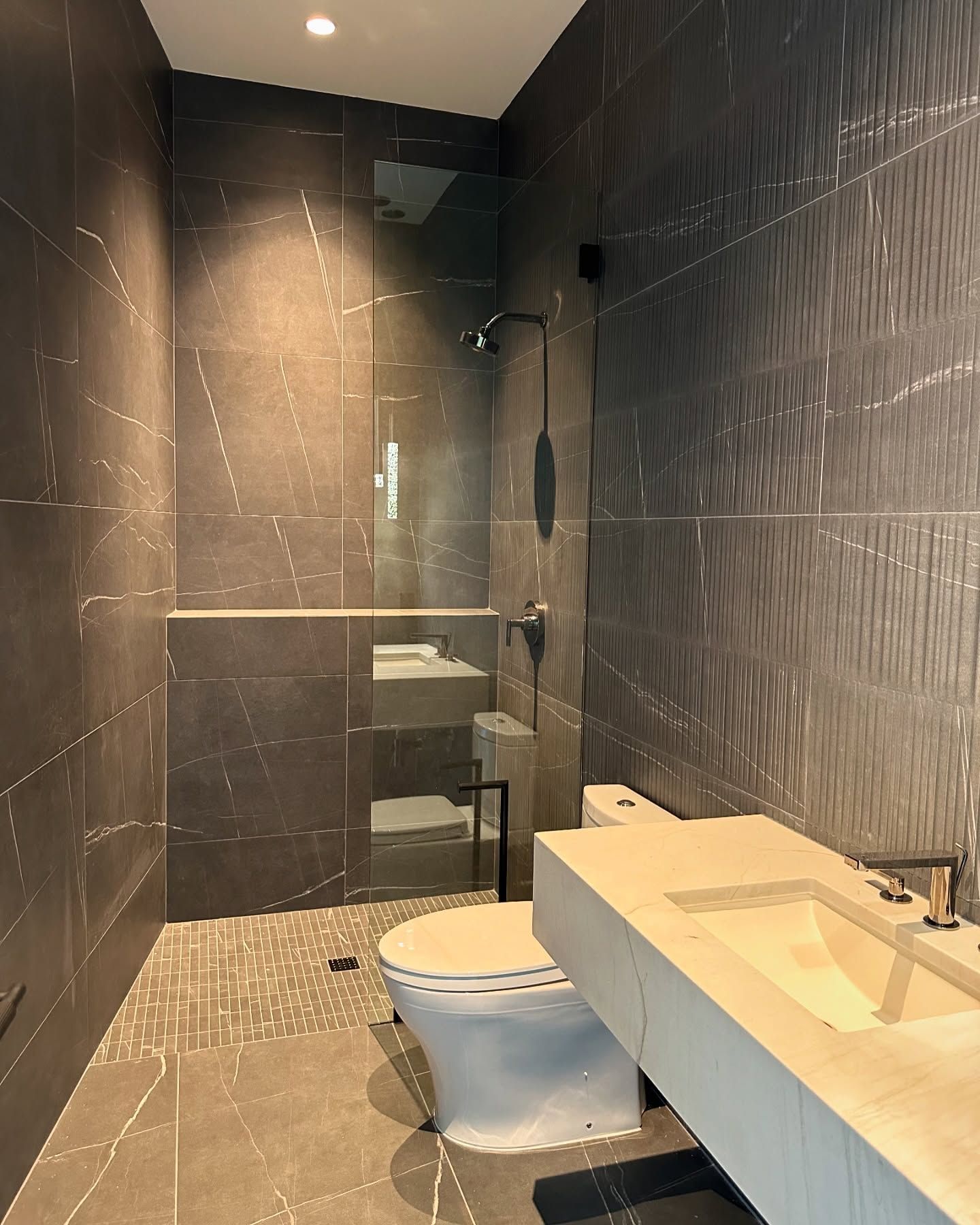 Modern bathroom with dark tile, shower, toilet, and a concrete sink.