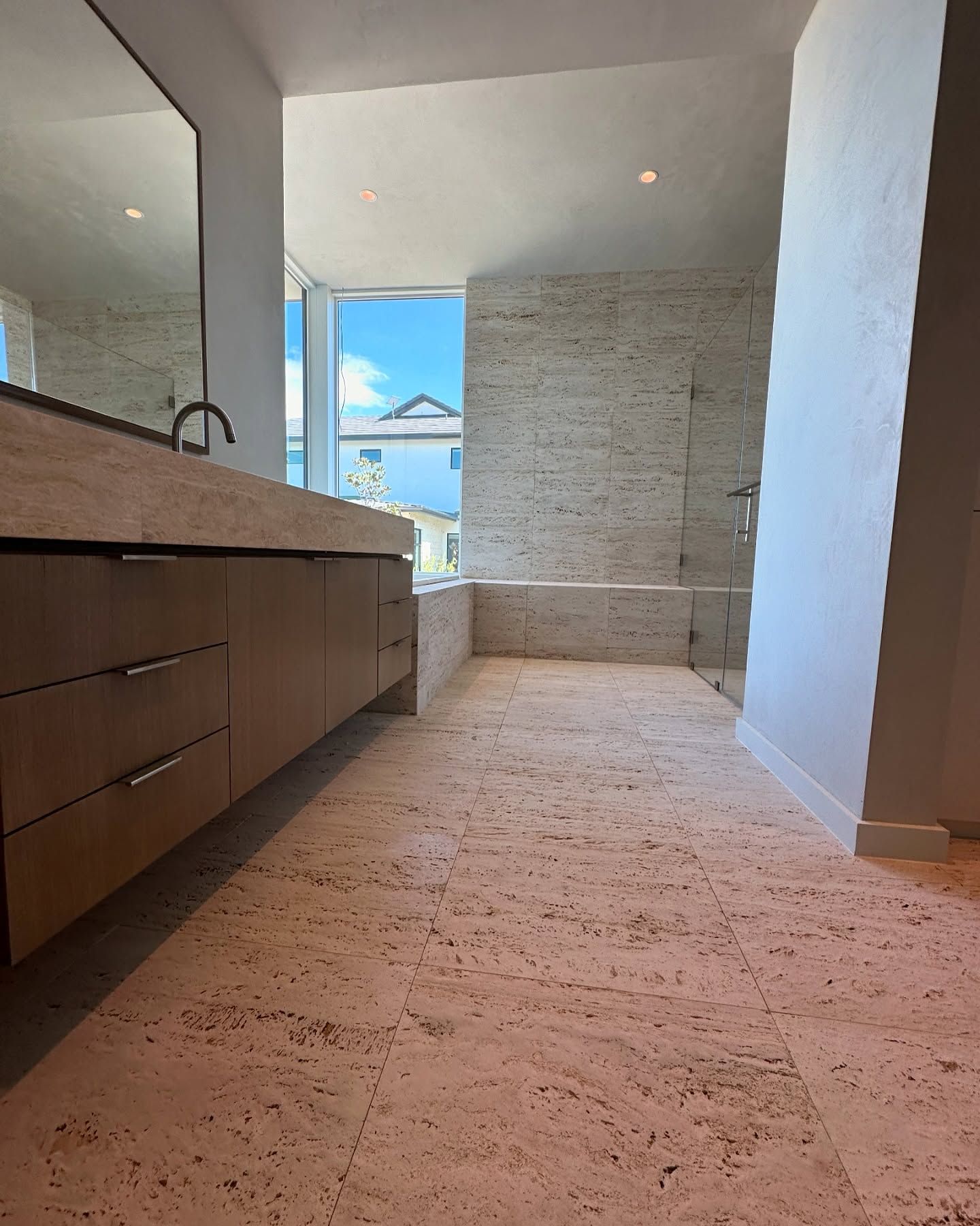 Bathroom with beige stone tile, vanity, and large window with a view.