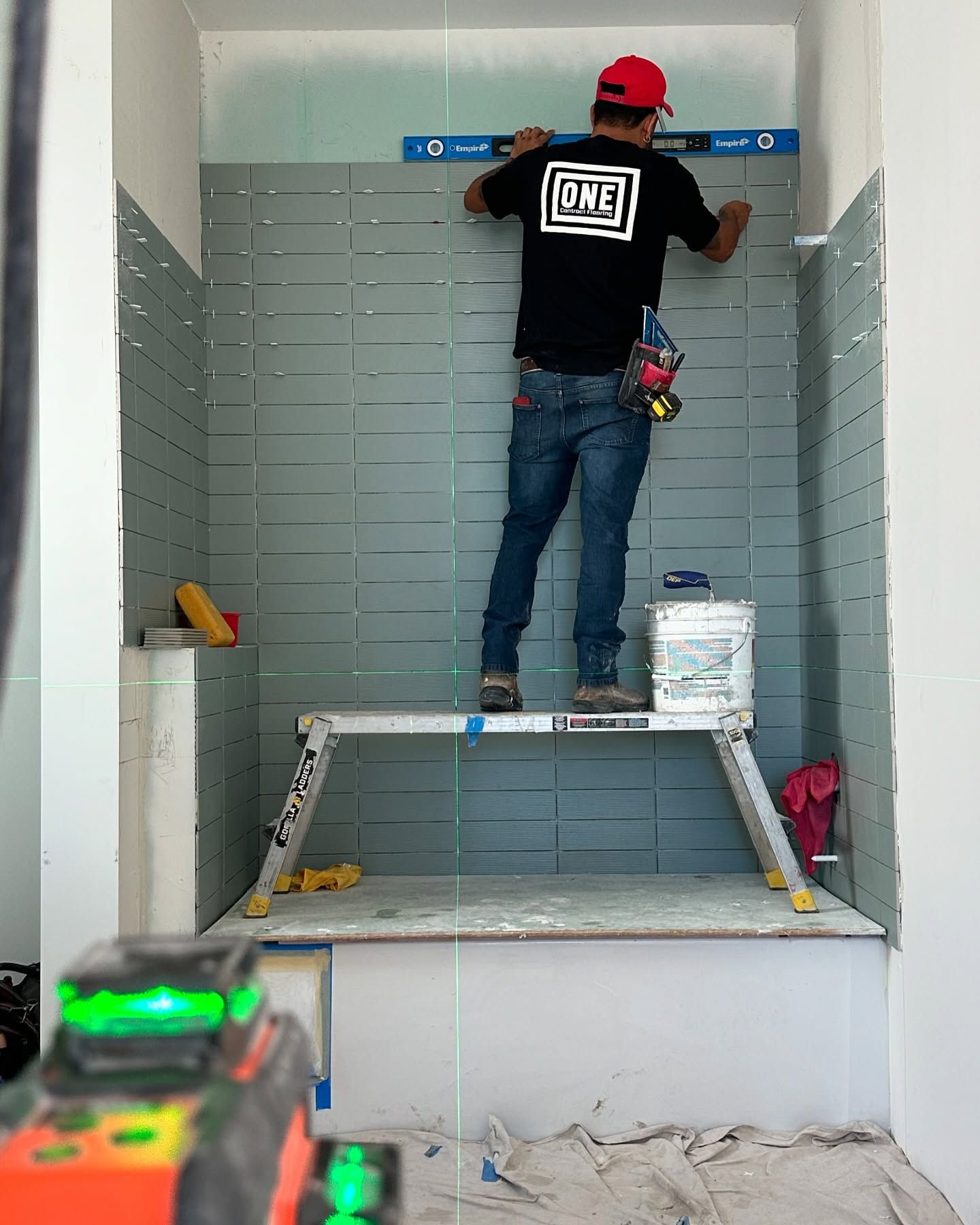 Person leveling tiles on a platform in a bathroom. Green laser level in the foreground.
