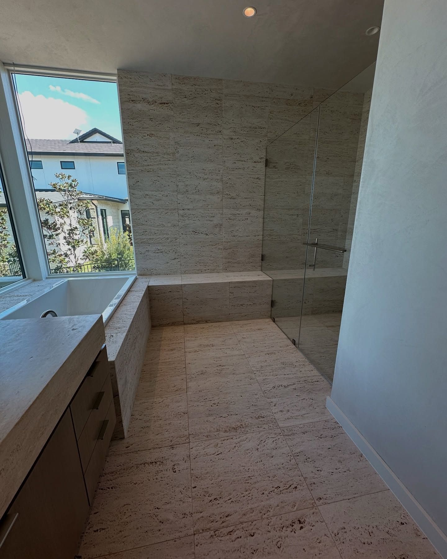 Bathroom with stone walls and floor, built-in sink and shower, and large window overlooking trees.