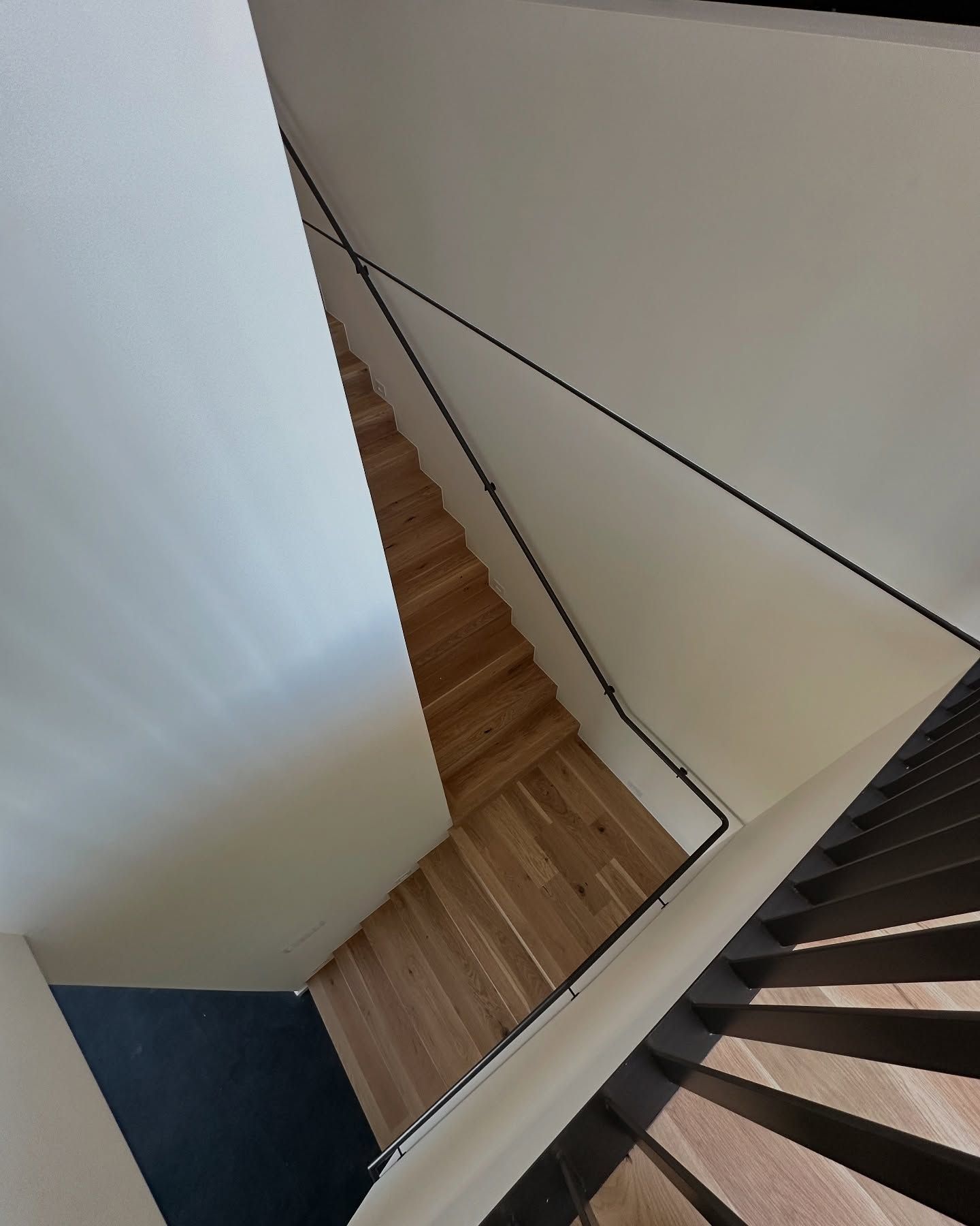 Stairwell: Wooden steps, white walls, black railing. Angled view.