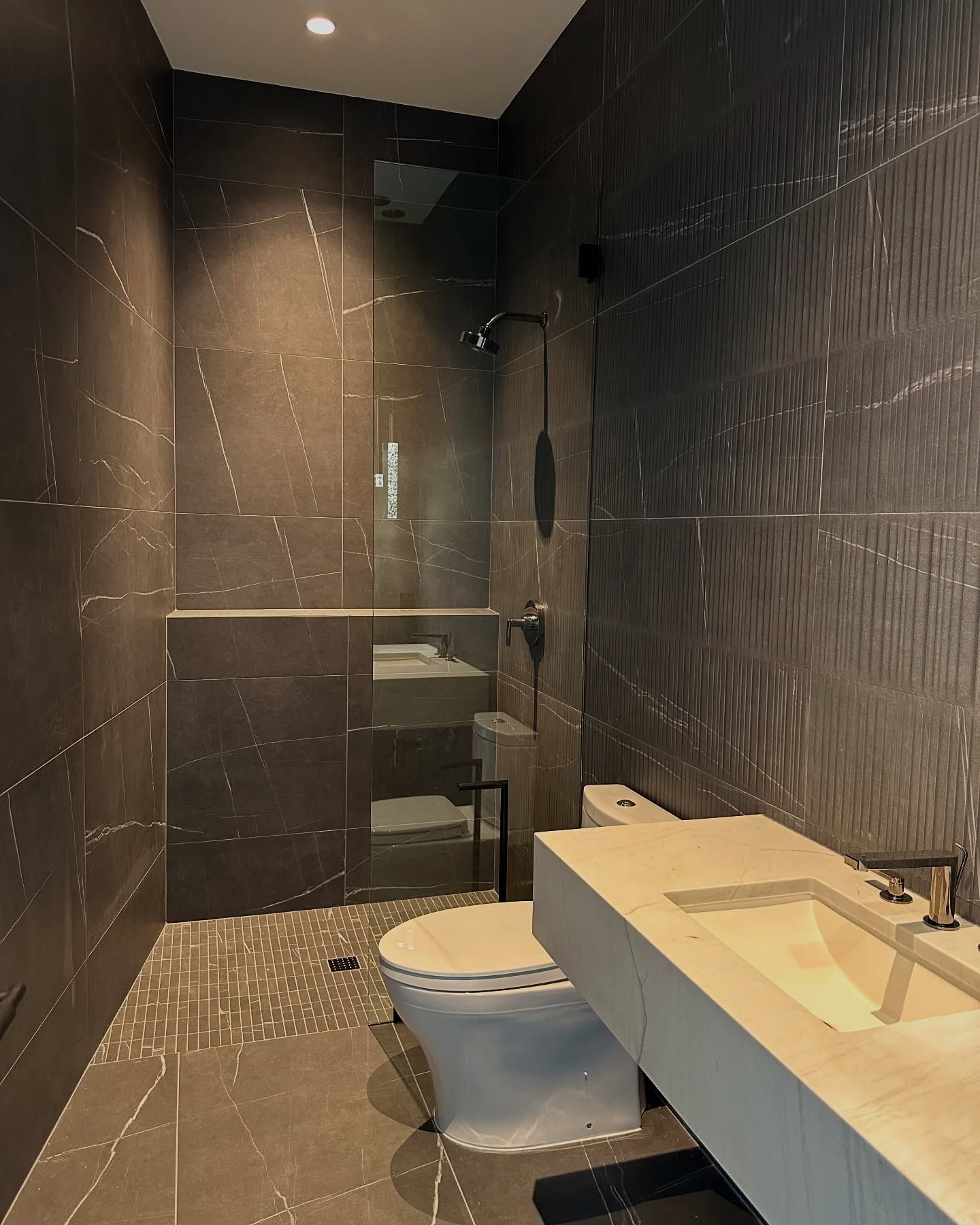 Modern bathroom with dark gray tile. Shower, toilet, and floating sink.