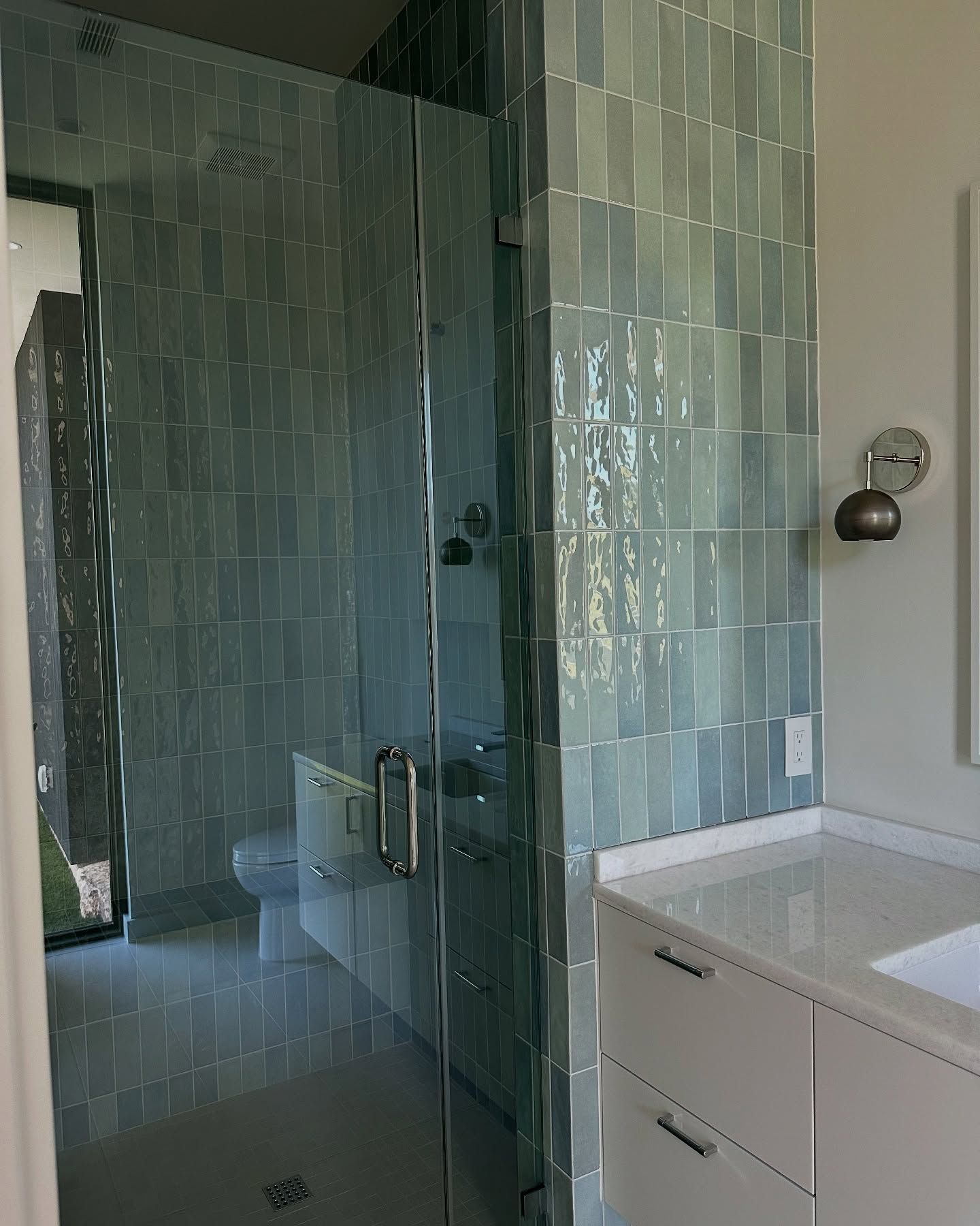 Bathroom with glass shower, blue tile walls, white vanity, and modern fixtures.
