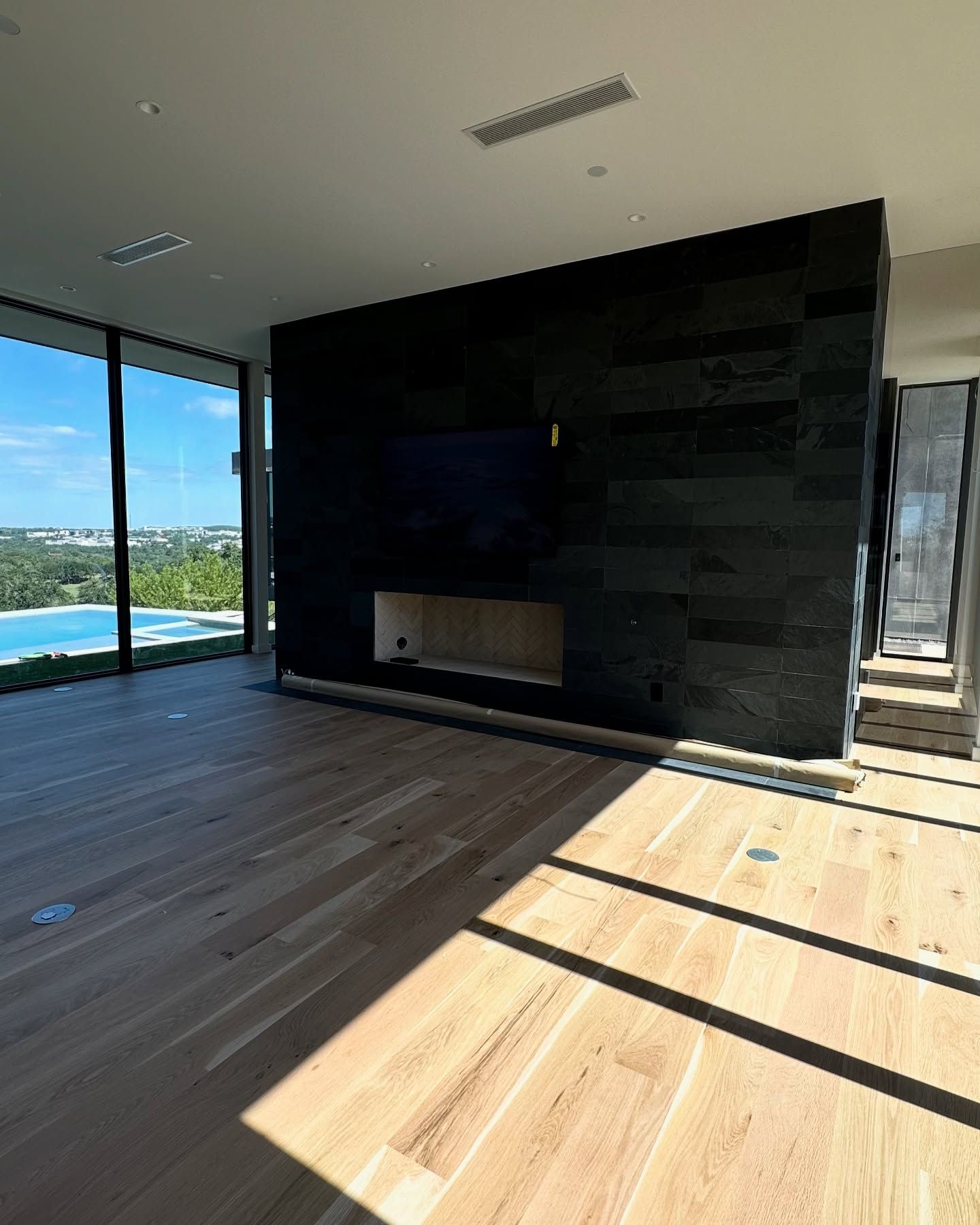 Modern living room with a black stone fireplace, wood floors, and floor-to-ceiling windows.