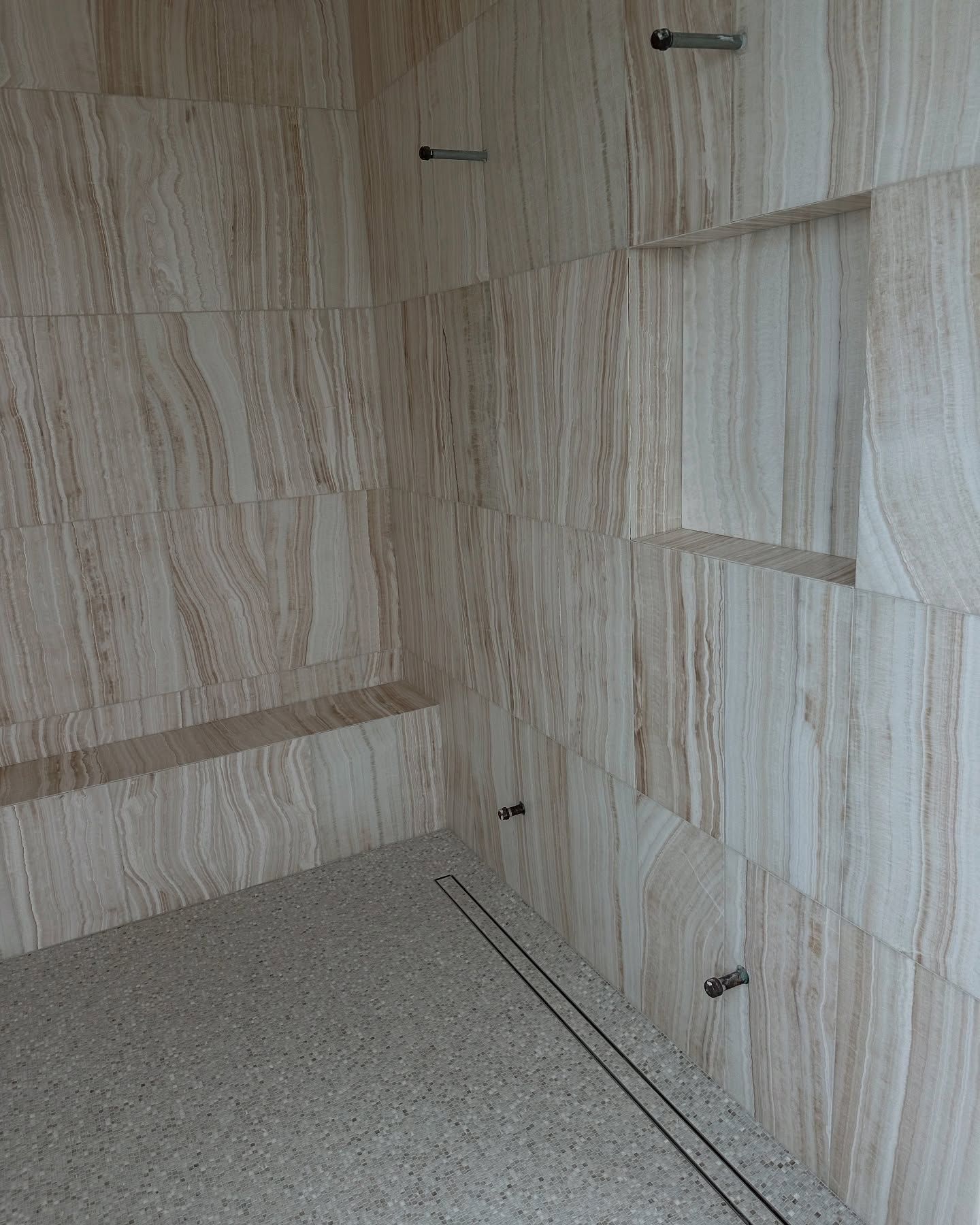 Corner of a tiled room. Light beige stone walls with embedded metal fixtures and a terrazzo floor.