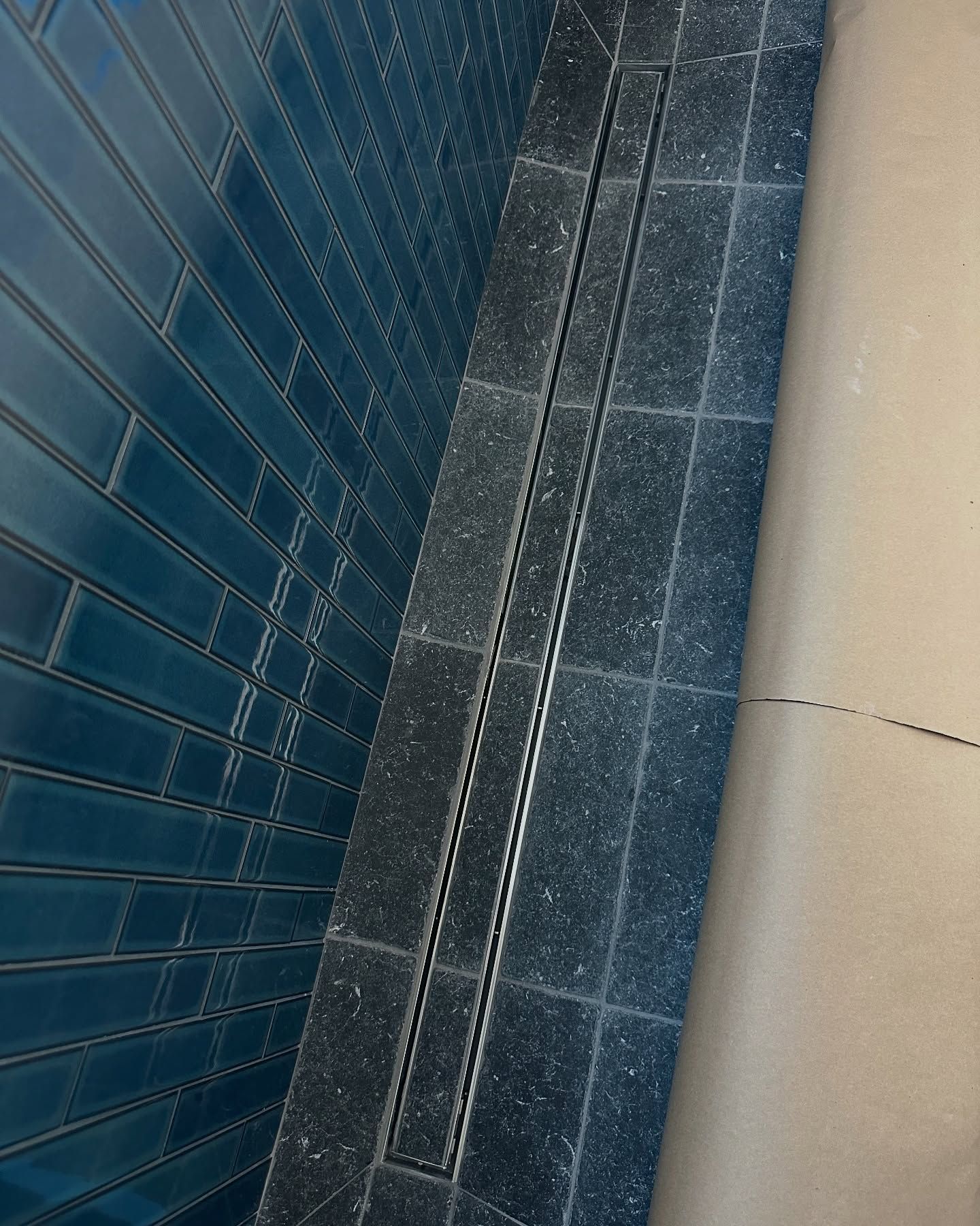 Blue tiled wall, dark tiled floor, linear drain, and beige floor create a shower area.