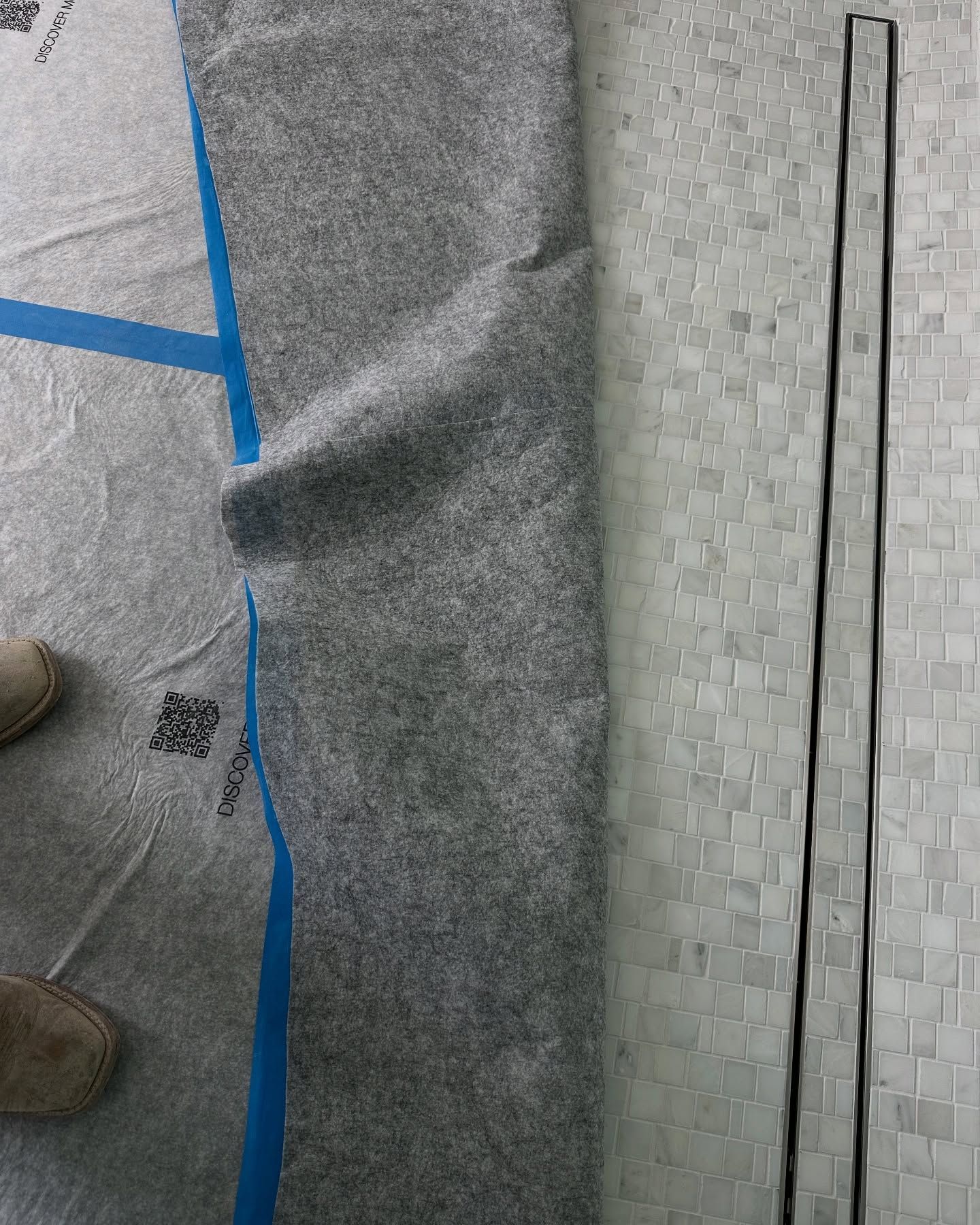 Gray fabric partially covering a patterned floor with blue tape, a black strip.