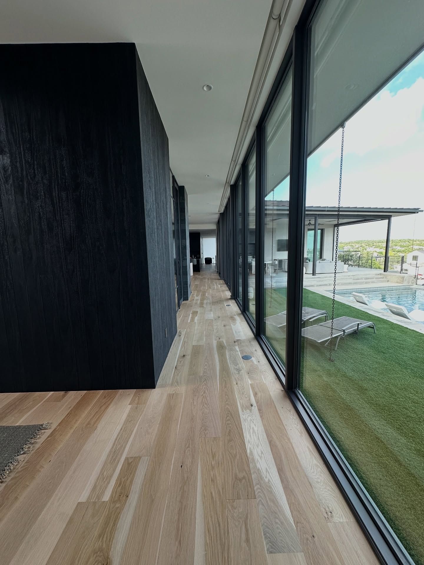 Long hallway with wood floor, black wall, and large windows overlooking a grassy yard.