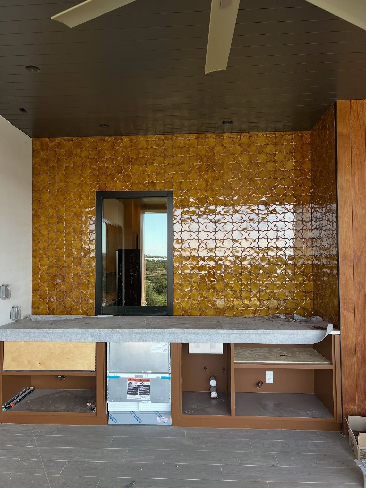 Interior with gold tiled wall, countertop, cabinets, and a black framed window.