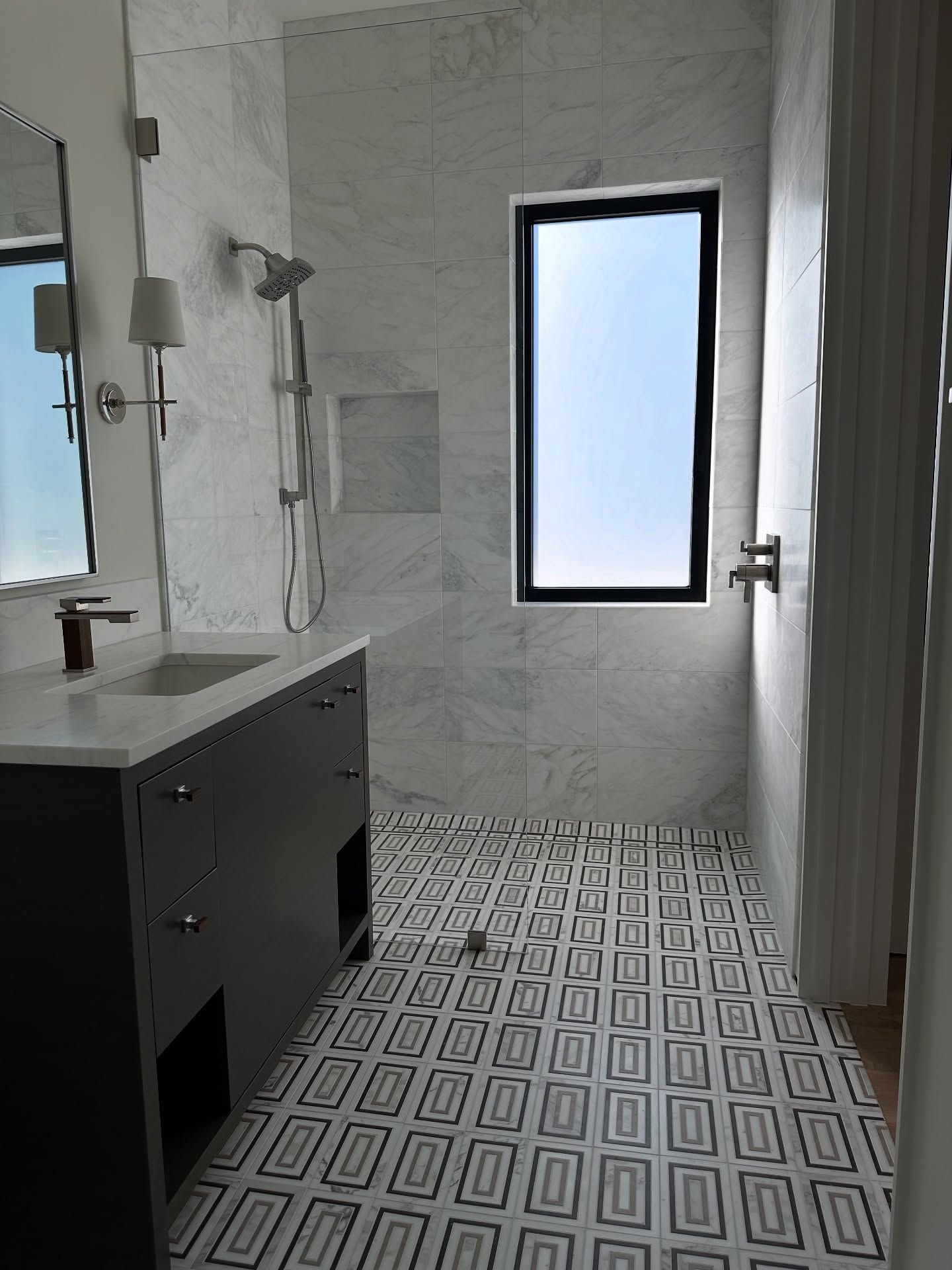 Modern bathroom with patterned floor, marble walls, dark gray vanity, and shower.
