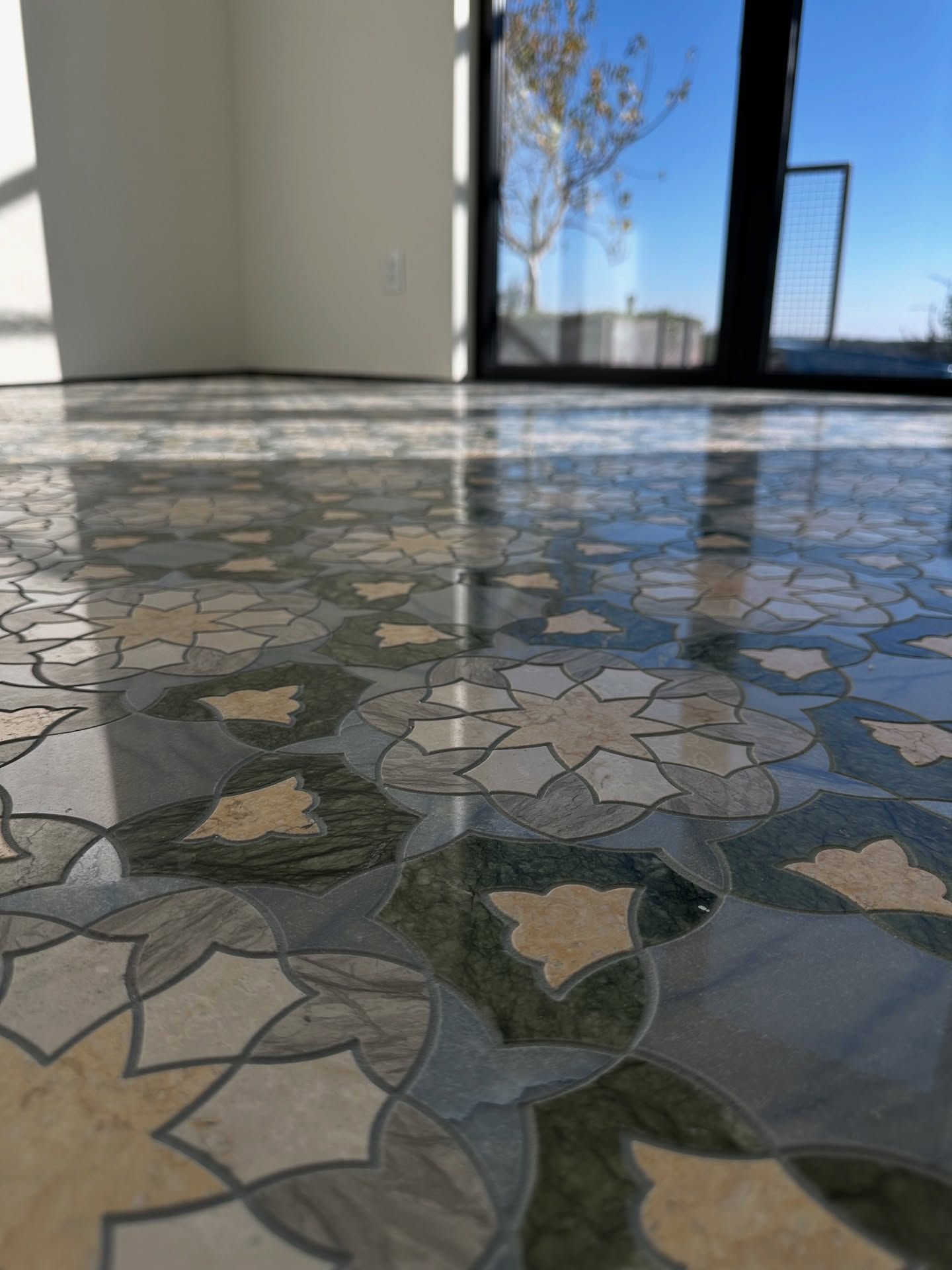 Close-up of a glossy patterned tile floor with a floral design, reflecting the sunlight from a window.