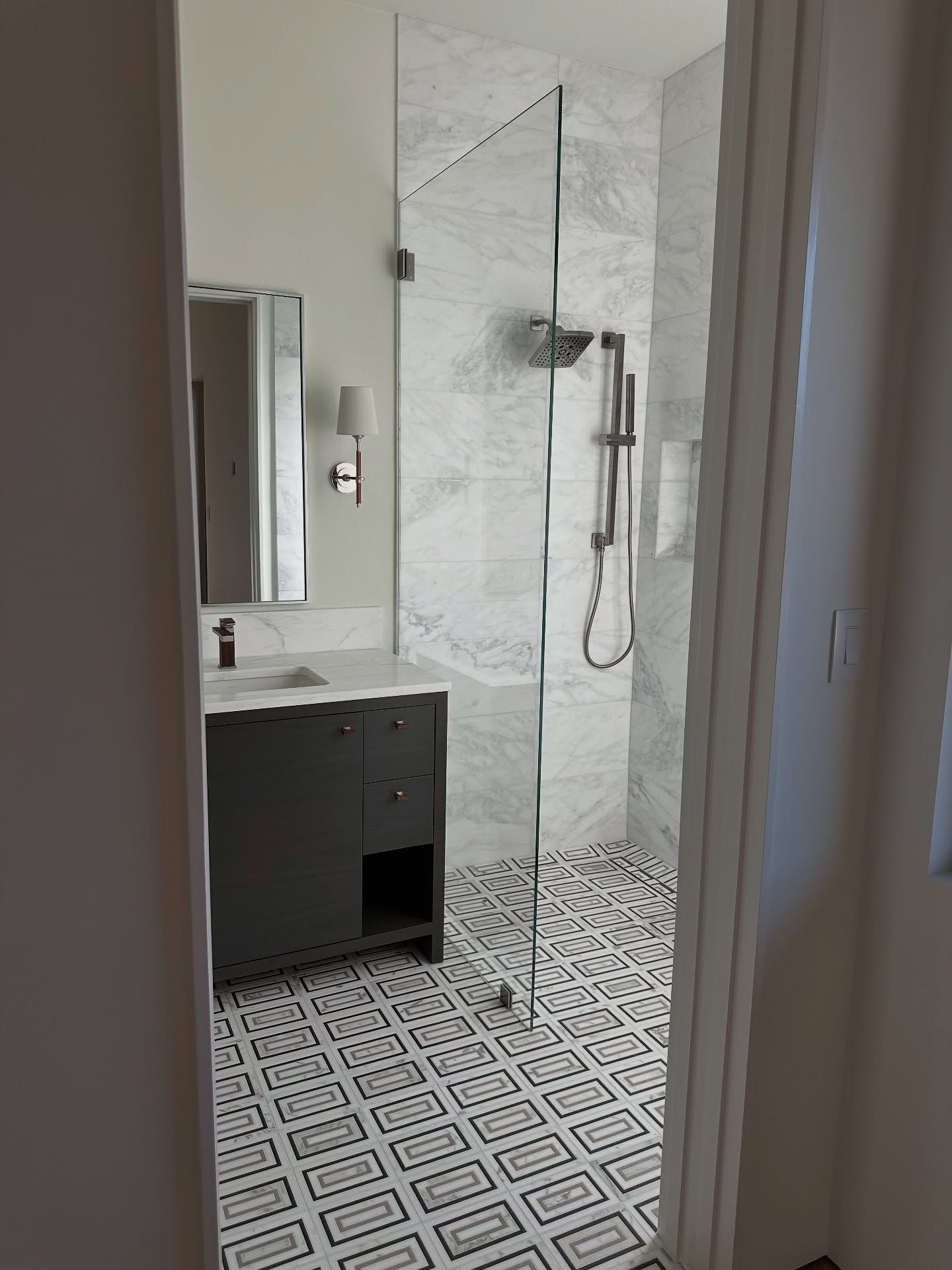 Bathroom with glass shower, gray vanity, and patterned floor. White marble shower wall.