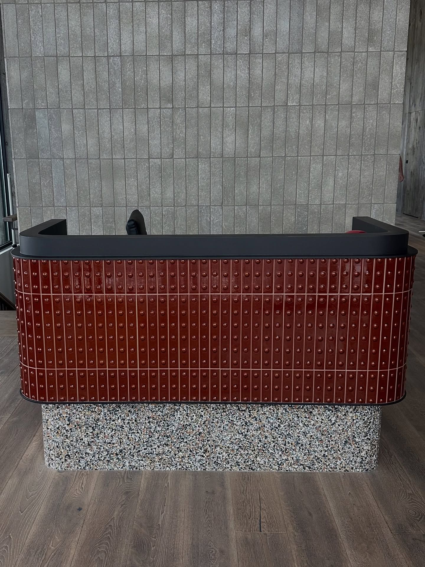 Red tiled reception desk with a textured stone base, against a gray brick wall.