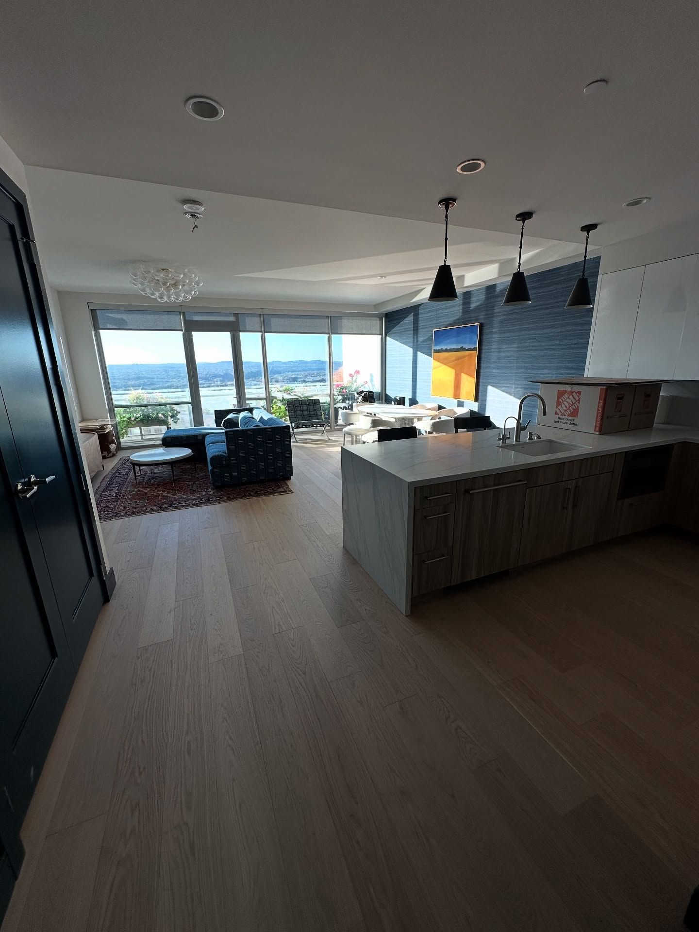 Open-concept living space with kitchen island, wood floors, and floor-to-ceiling windows overlooking a body of water.