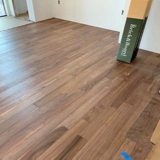 Newly installed hardwood floor in a room with white walls; a box of flooring materials sits on the floor.