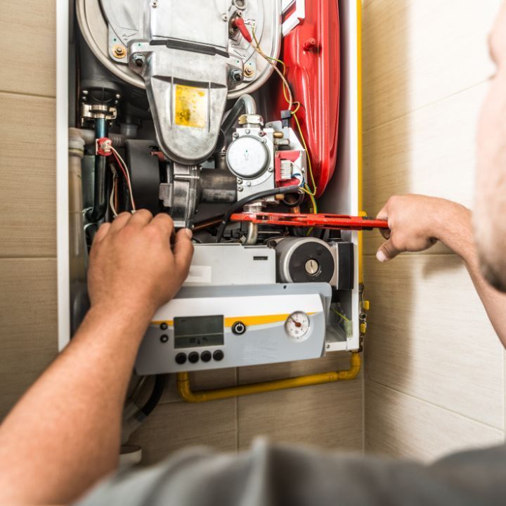 A technician uses a red wrench to repair the internal components of a wall-mounted gas boiler.