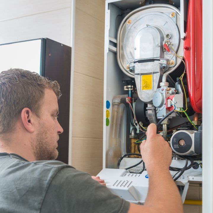 A technician in a grey shirt inspecting the internal components of a wall-mounted gas boiler.