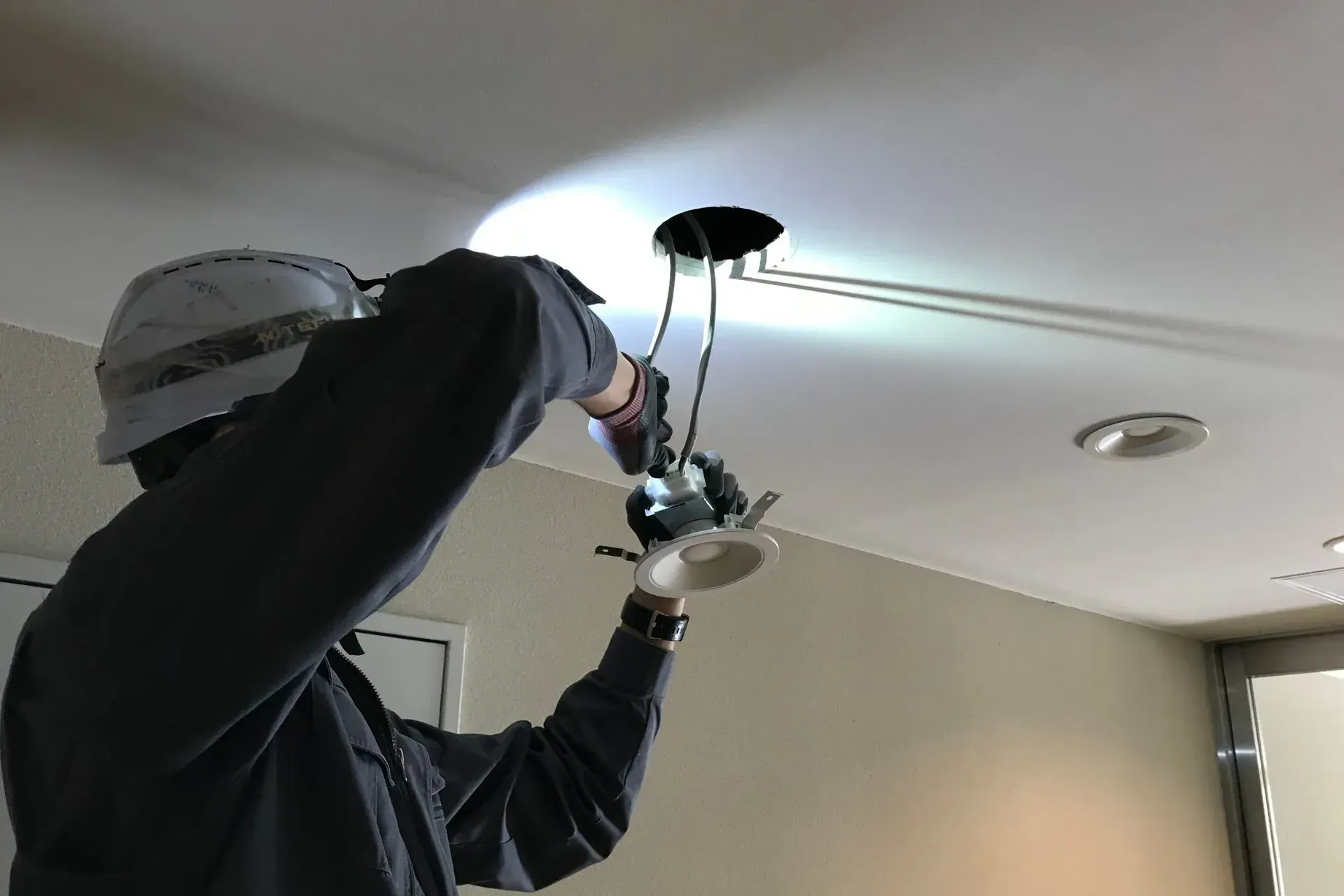 Person installs a recessed light fixture in a ceiling, wires exposed. Electrical Services Plymouth MI