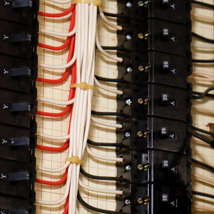 Electrical panel with red, white, and black wires connected to black circuit breakers, close-up. Electrician Services in Livonia MI