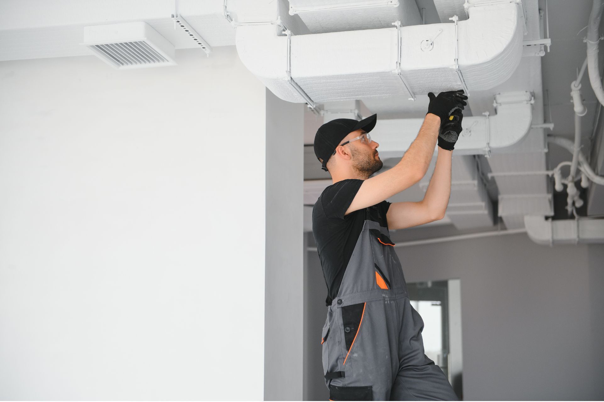 HVAC technician in overalls installs ductwork on a ceiling. AC Installation in Plymouth, MI