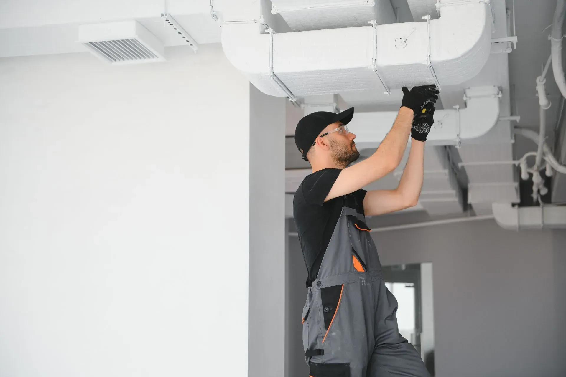 HVAC technician in overalls installs ductwork on a ceiling. AC Installation in Plymouth, MI
