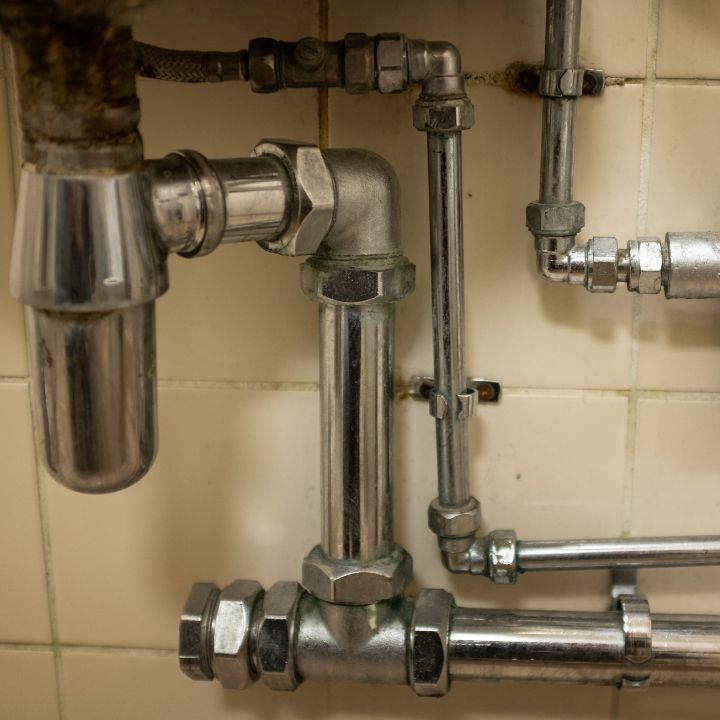 Close-up of chrome plumbing pipes against cream-colored tile. Plumbing Services in Livonia