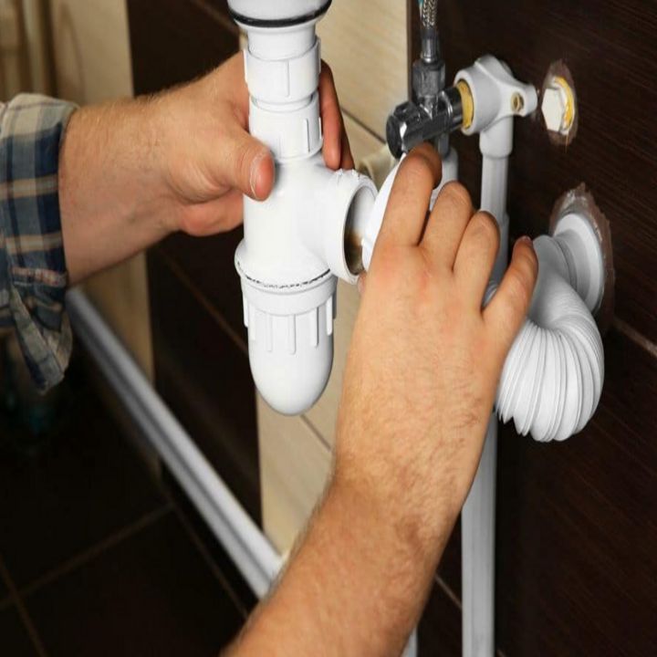 Person's hands assembling white plumbing pipes under a sink.