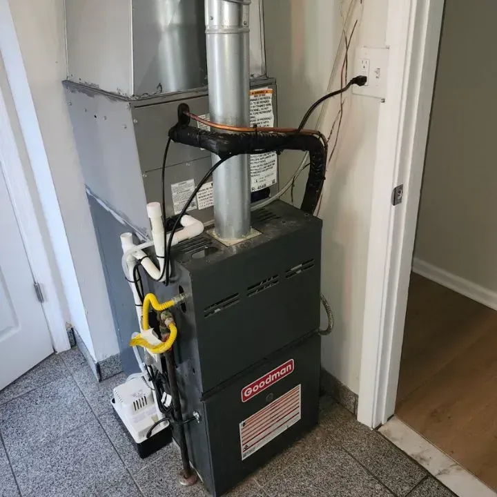 Black furnace with silver vent pipes in a small hallway beside a doorway and carpeted floor.