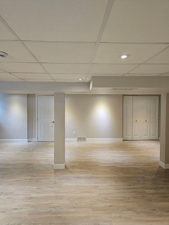 Pièce vide au sous-sol avec portes à panneaux blancs, une colonne de soutien et un sol en moquette beige