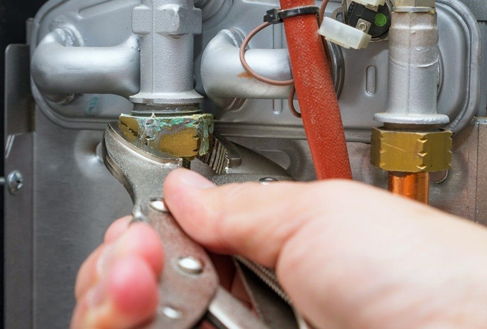 A Person's Hand Using Pliers to Tighten a Fitting on a Gas Boiler — Rob Powell Plumbing Pty Ltd in Byron Bay, NSW
