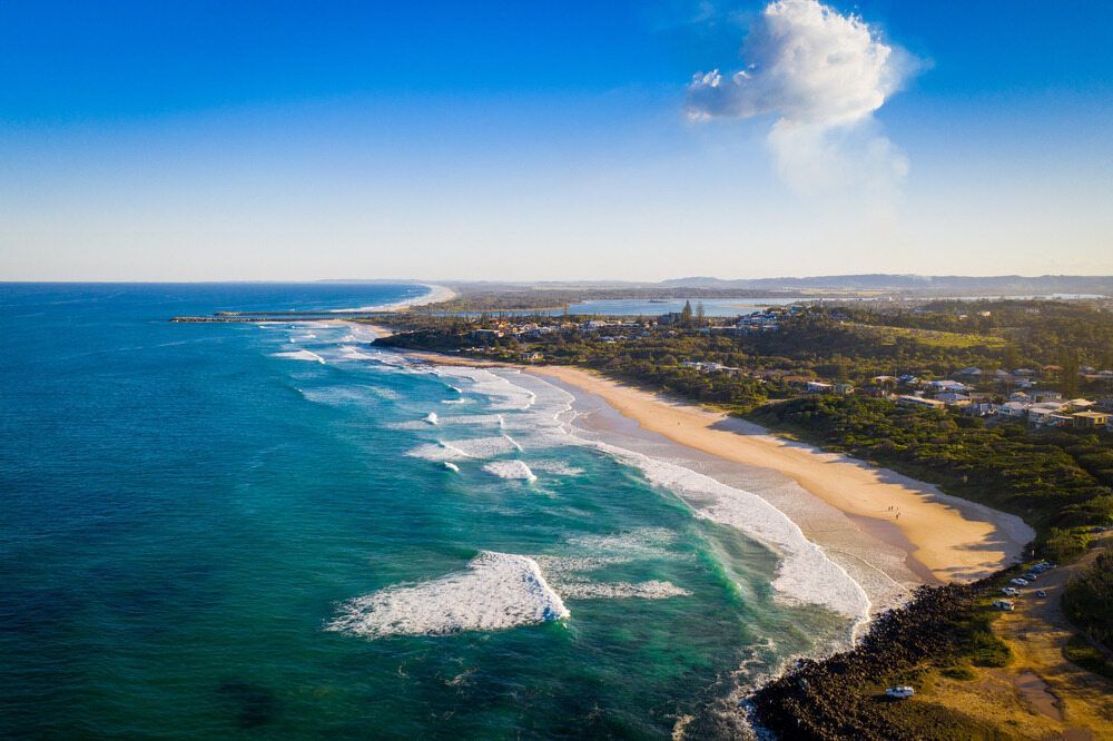 Aerial View of a Sunny Beach With Waves Crashing on the Shore and Clear Blue Water — Rob Powell Plumbing Pty Ltd in Ballina, NSW