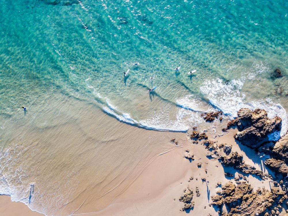 Beach With Clear Turquoise Water, Surfers, and Rocky Shore. Sandy Beach on the Lower Left — Rob Powell Plumbing Pty Ltd in Byron Bay, NSW