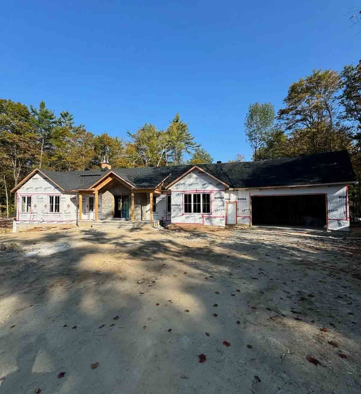 Maison de plain-pied avec un grand garage, un bardage blanc et un toit foncé, sur un terrain boisé.