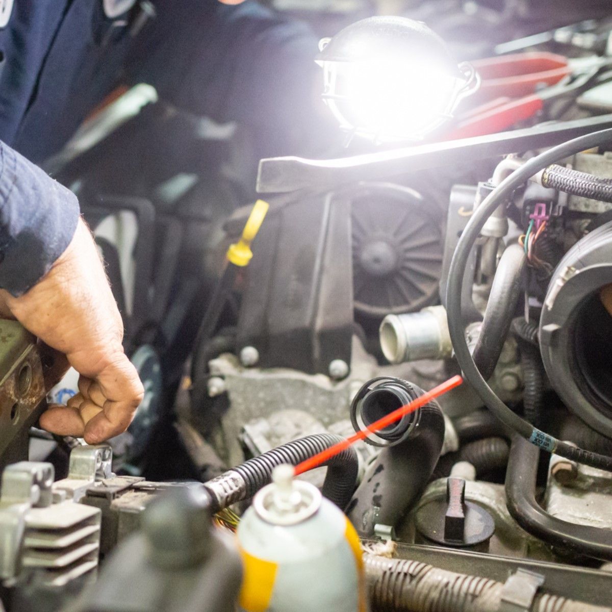 Mechanic working on car engine, using a flashlight and spray can.