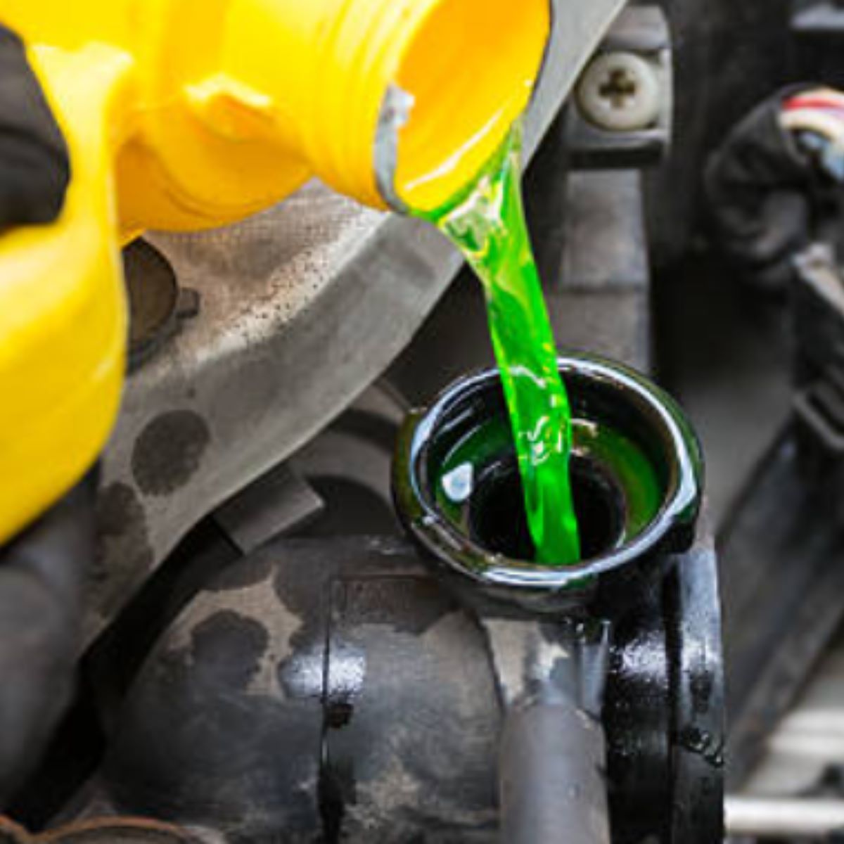 Green coolant being poured from a yellow jug into a car radiator.