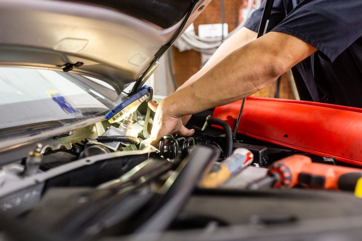 Mechanic working on a car engine bay, illuminated by a work light.
