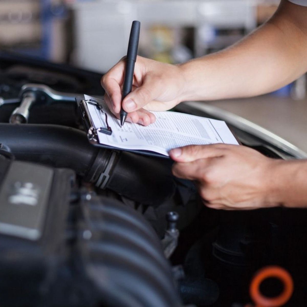 Mechanic inspecting car engine, writing on clipboard.