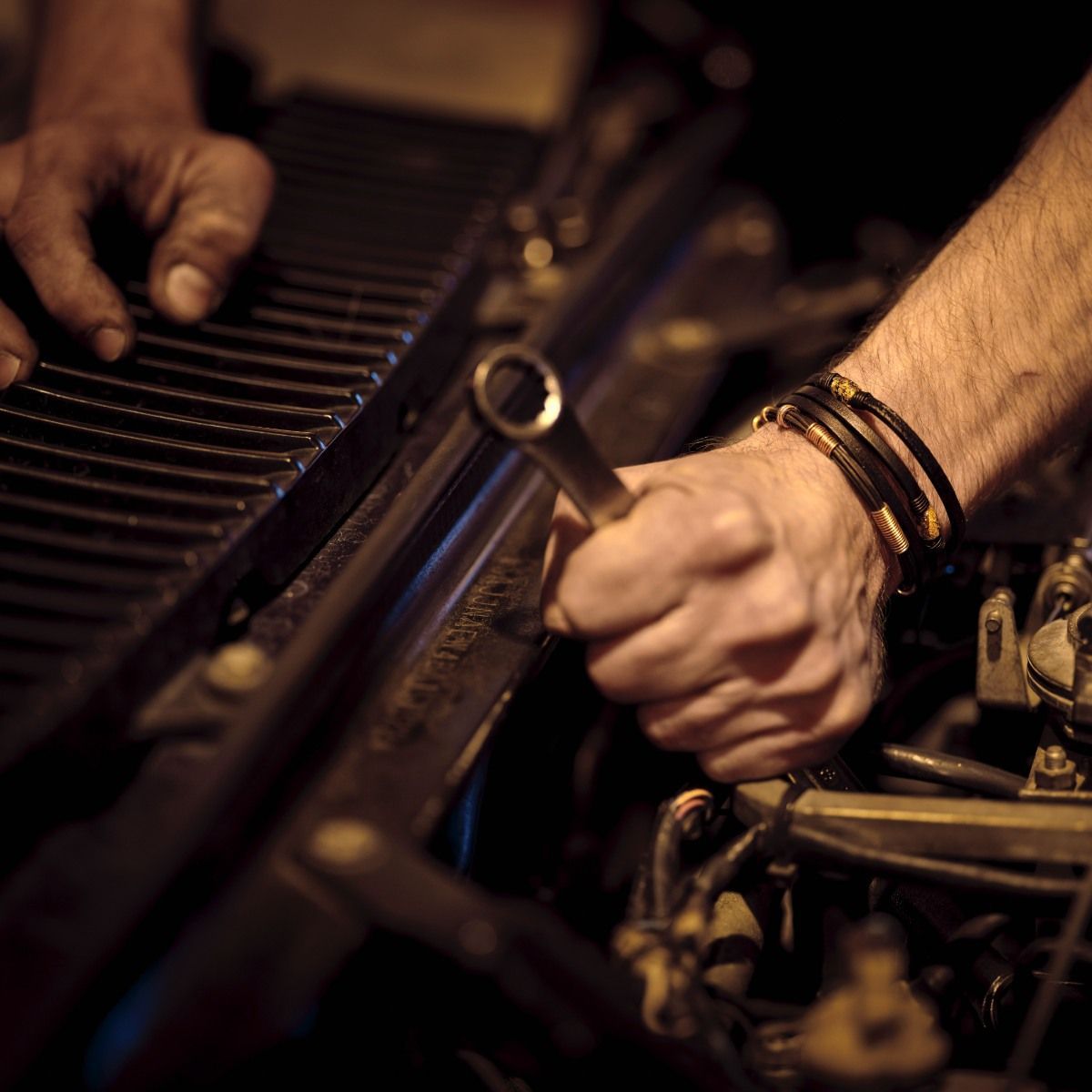 Hands with wrench working on a car engine.